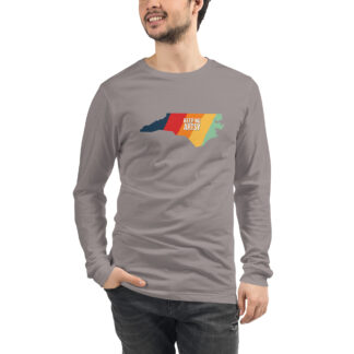 Picture of a man wearing a gray long sleeved t-shirt printed with NC state shape that has five vertical stripes - blue, red, orange, yellow and light green. Text in the center says "Keep NC Artsy".
