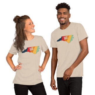Picture of a man and a woman wearing cream colored t-shirt printed with NC state shape that has five vertical stripes - blue, red, orange, yellow and light green. Text in the center says "Keep NC Artsy".