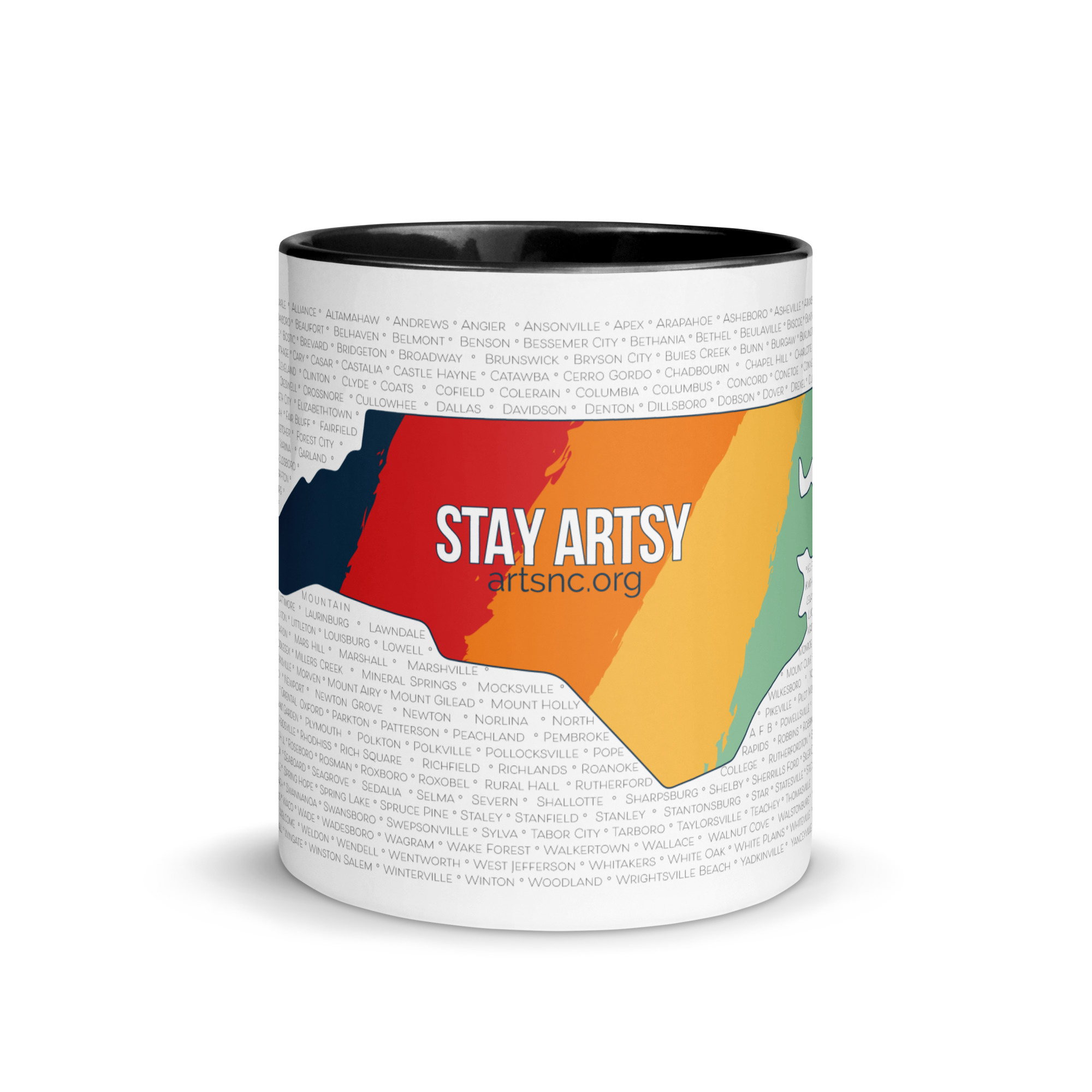 A white mug with black inside and a black handle. The outside of the mug is printed with NC state shape that has five vertical stripes - blue, red, orange, yellow and light green. Text in the center says "Stay Artsy". In the background are rows of NC county and city names.