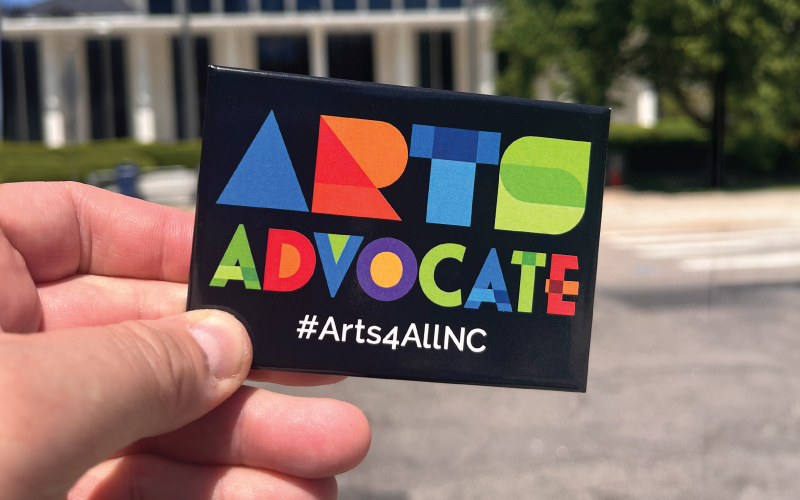 Picture of a hand holding a button that says Arts Advocate