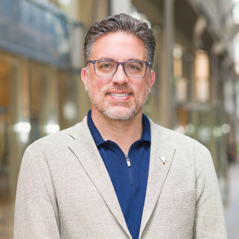 Picture of Jamie Bennett, a white man with brown hair and a beard. He is wearing glasses and a dark blue shirt and tan blazer.